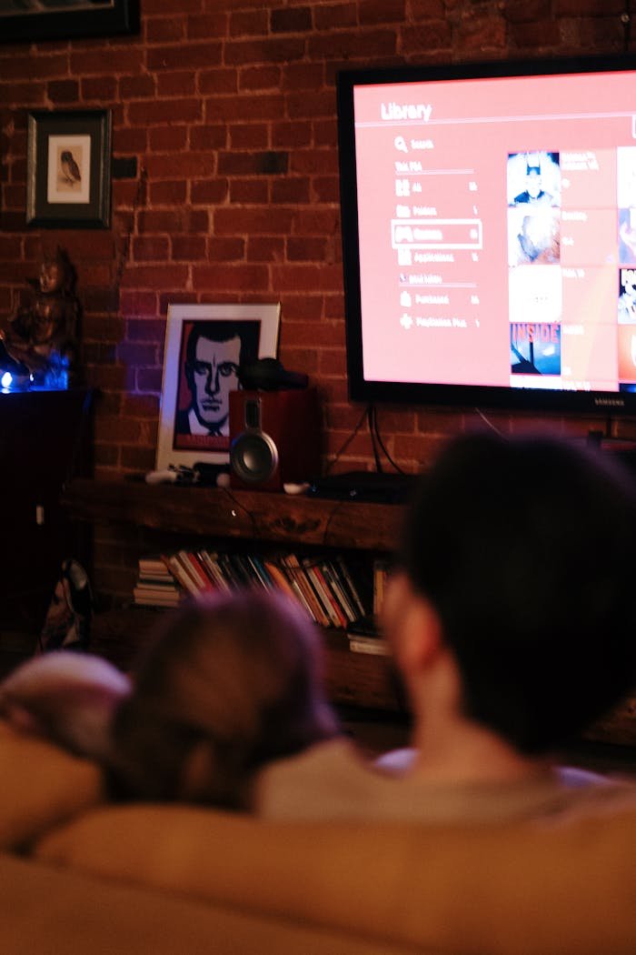 A couple snuggles on the couch watching TV in a cozy brick-walled living room.